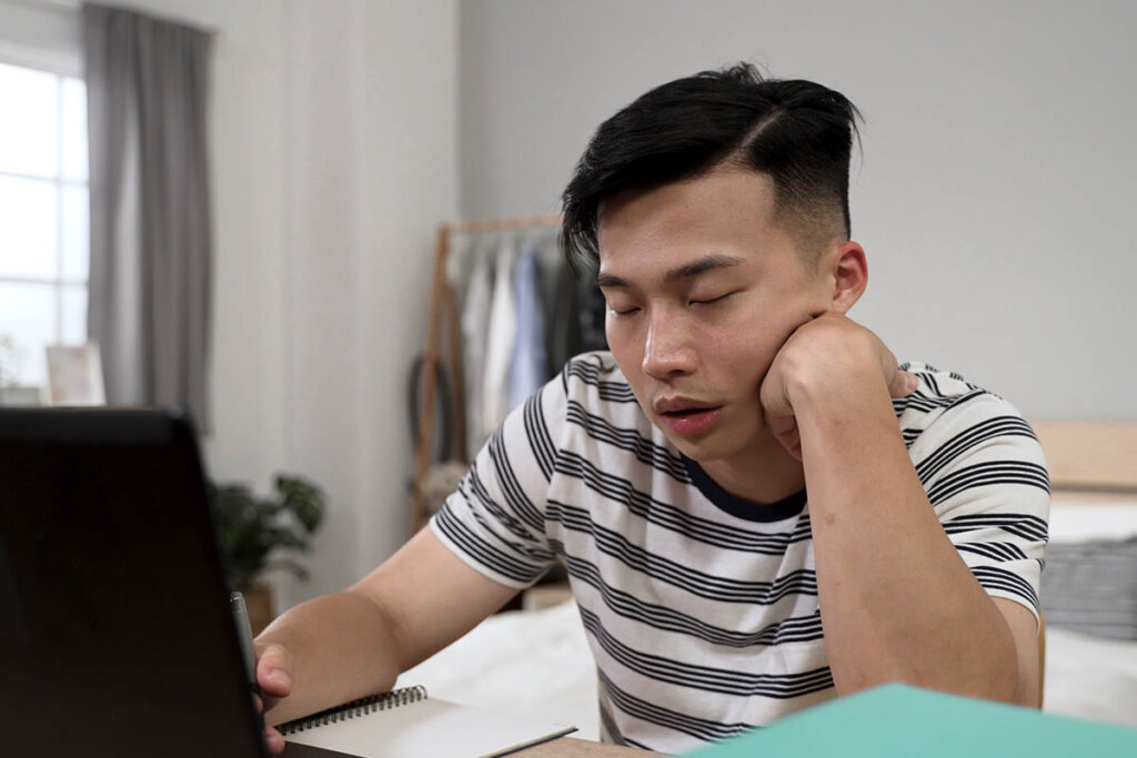 a man in a stripe shirt sits with his head resting on his hand and arm appearing to be nodding off on heroin