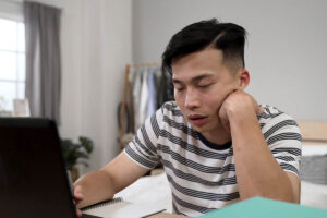 a man in a stripe shirt sits with his head resting on his hand and arm appearing to be nodding off on heroin