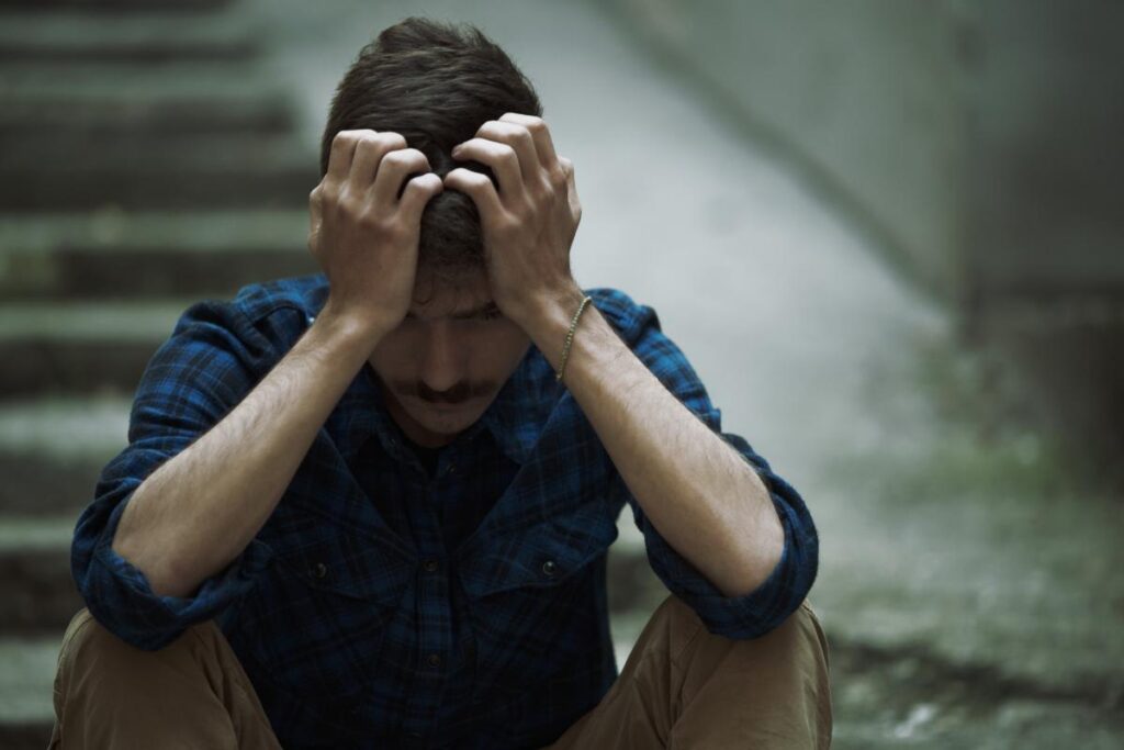 a man sits outside on stairs with his palms to his head struggling with the question is shooting crack safe