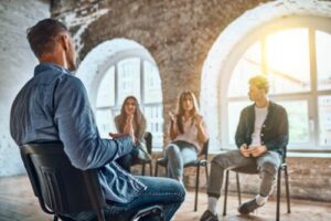 a man is talking to three other people while participating in his addiction therapy program