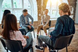 a group of people sit around in a circle at a mental health treatment center discussing their thoughts in group therapy