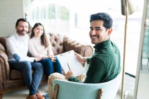 a therapist smiles at camera while a couple sits together on a couch in a family integration therapy program