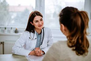 a doctor sits in front of a patient at her desk discussing medication assisted treatment programs