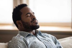 a man sits on a couch meditating during his mindfulness and meditation therapy program