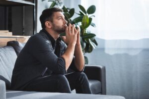 a man sits on a couch and thinking hard about the long-term effects of anxiety