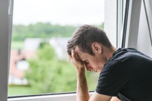 a man sits near window with hand on his head distraught over the signs of heroin addiction