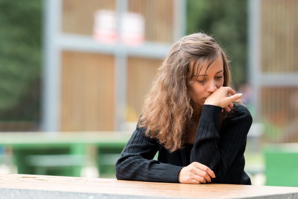 woman sits outside at a table distraught over learning about the signs of meth use