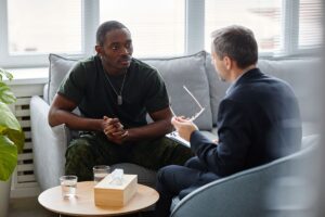 a man sits on a couch while talking to a therapist about a veterans program for addiction