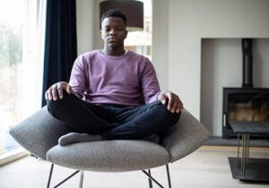 man sits on a chair with his legs crossed and meditating after learning how to in holistic addiction therapy