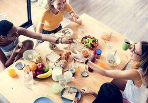 four women are sitting down at a table sharing breakfast at a sober living program