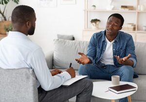 a man sits on a couch across from his therapist talking about his trauma during his trauma therapy program