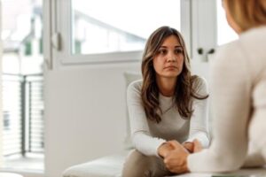 a woman sits talking to a person in a 12-step addiction treatment program