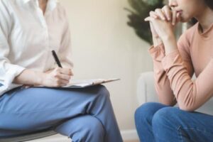 a person takes notes while another person sits and talks in an anger management therapy program