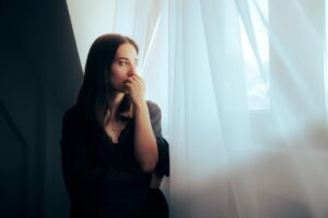 a woman stands near a window looking out concerned with learning about preventing relapse during the holidays