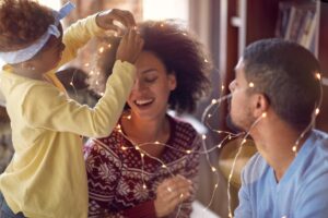 a small child puts holiday lights around her parents while her parents think about how to have a sober new year's eve