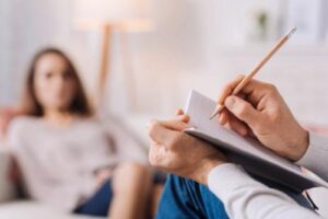 a therapist writes down notes while listening to a female patient in a psychotherapy program
