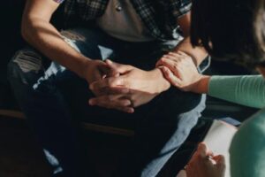 photo of a person's hands interlocked on their lap while another person touches their arm while consoling them in acceptance and commitment therapy program
