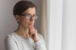 a woman holds her hand to her chin while staring out a window wondering about the connection between cocaine and anxiety