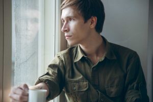 man holds coffee cup while looking out the window in the distance thinking about the effects of unresolved anger