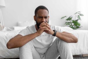 a man sits on the ground near his bed in deep thought about the psychological effects of meth