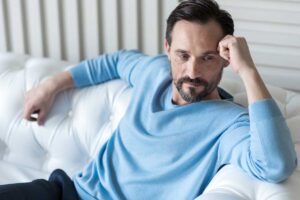 man sits on a couch with head resting on his raised arm while looking away thinking about the signs of a personality disorder