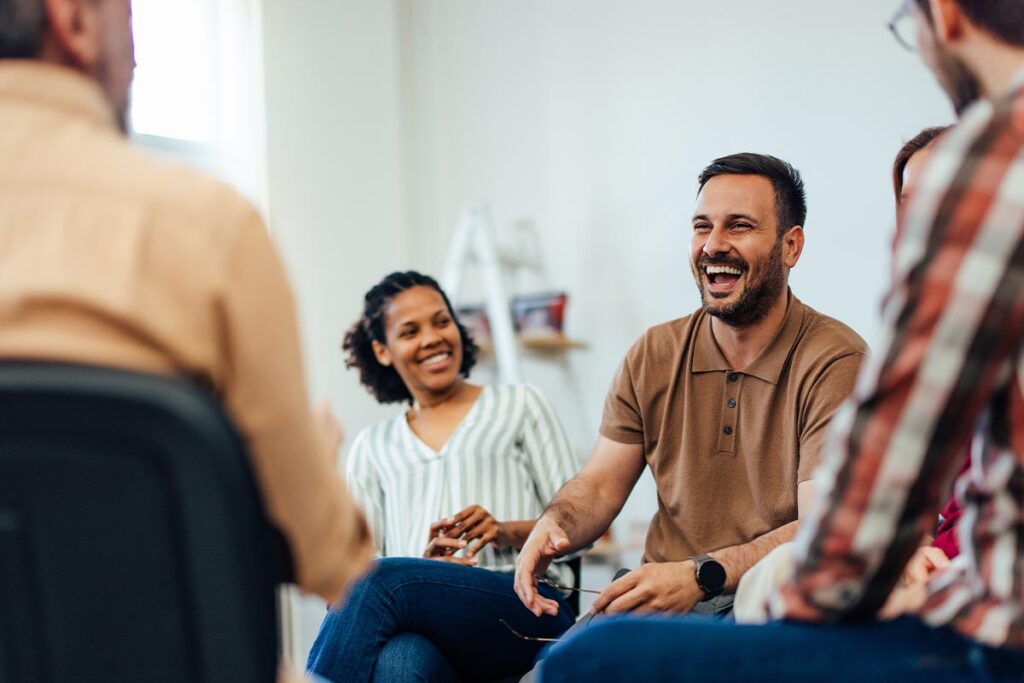 a group of people sit in a group therapy session while one person asks does outpatient rehab really work