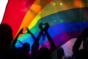 group of people stand under a rainbow flag in the dark showing support for people dealing with substance abuse in the LGBTQ+ community