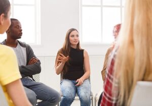 a woman is talking and raises her hand in her group therapy session for her polysubstance abuse treatment