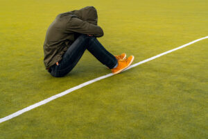 a person sits on football field with their hood over their head and is struggling with fentanyl overdose symptoms