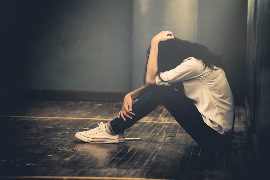 a young person sits on the ground holding their head to their knees while thinking about the dangers of taking ecstasy