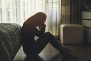 person sits on the floor and leans their back on a bed while leaning over struggling with the signs of cocaine use