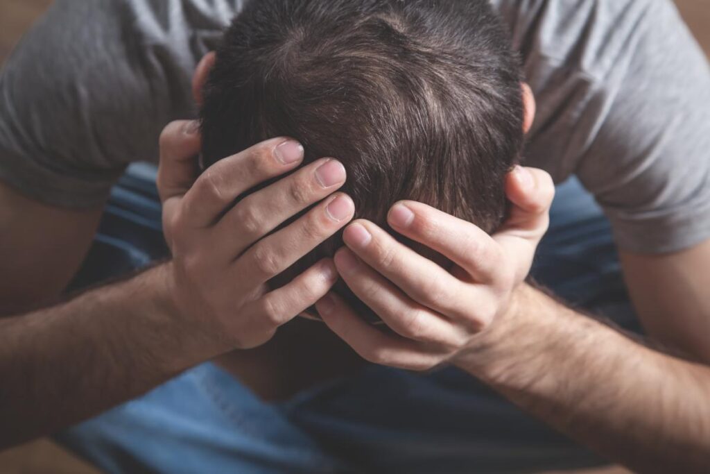 man leans over hold his head and displaying signs of emotional trauma in adults