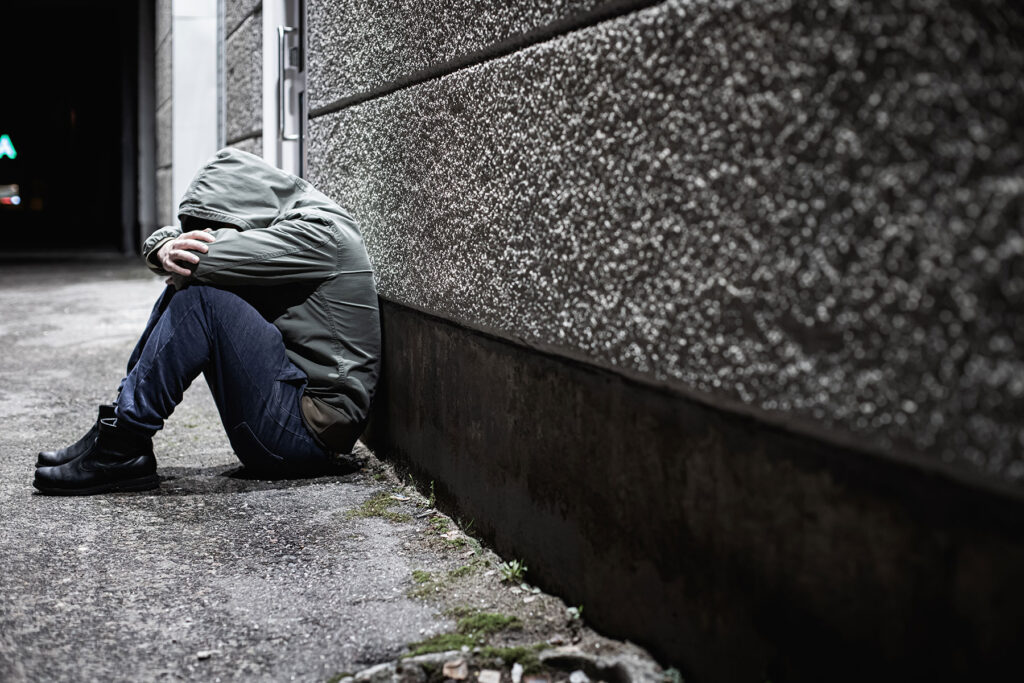 man in a hoodie sits on the ground and leans against a wall wondering how long does meth stay in your system