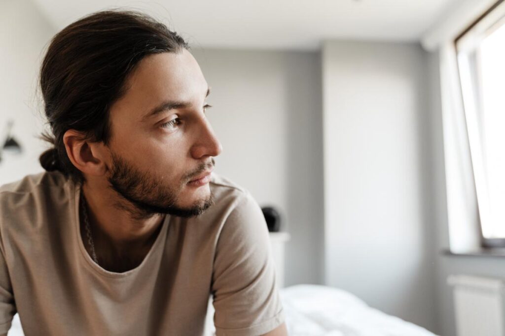 man with beard sits and looks to the side thinking about oxycontin and its side effects