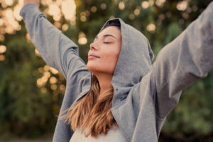 woman wearing a hoodie holds her hands up and embraces life after rehab