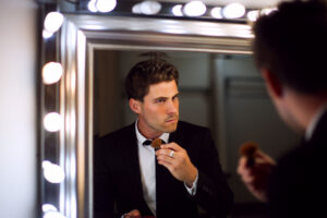 a man looks at himself in a mirror and straightens his bow tie thinking about the different types of narcissism
