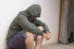 an upset man with a hoodie leans against a wall and thinks about the connection between heroin and depression