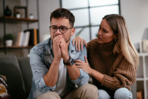 an upset man sits and holds his hands to his mouth wondering how to help someone with a drinking problem while a friend sits next to him and tries to console him