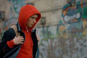 a young male adult wearing a backpack and a red hoodie walks while thinking about meth's side effects